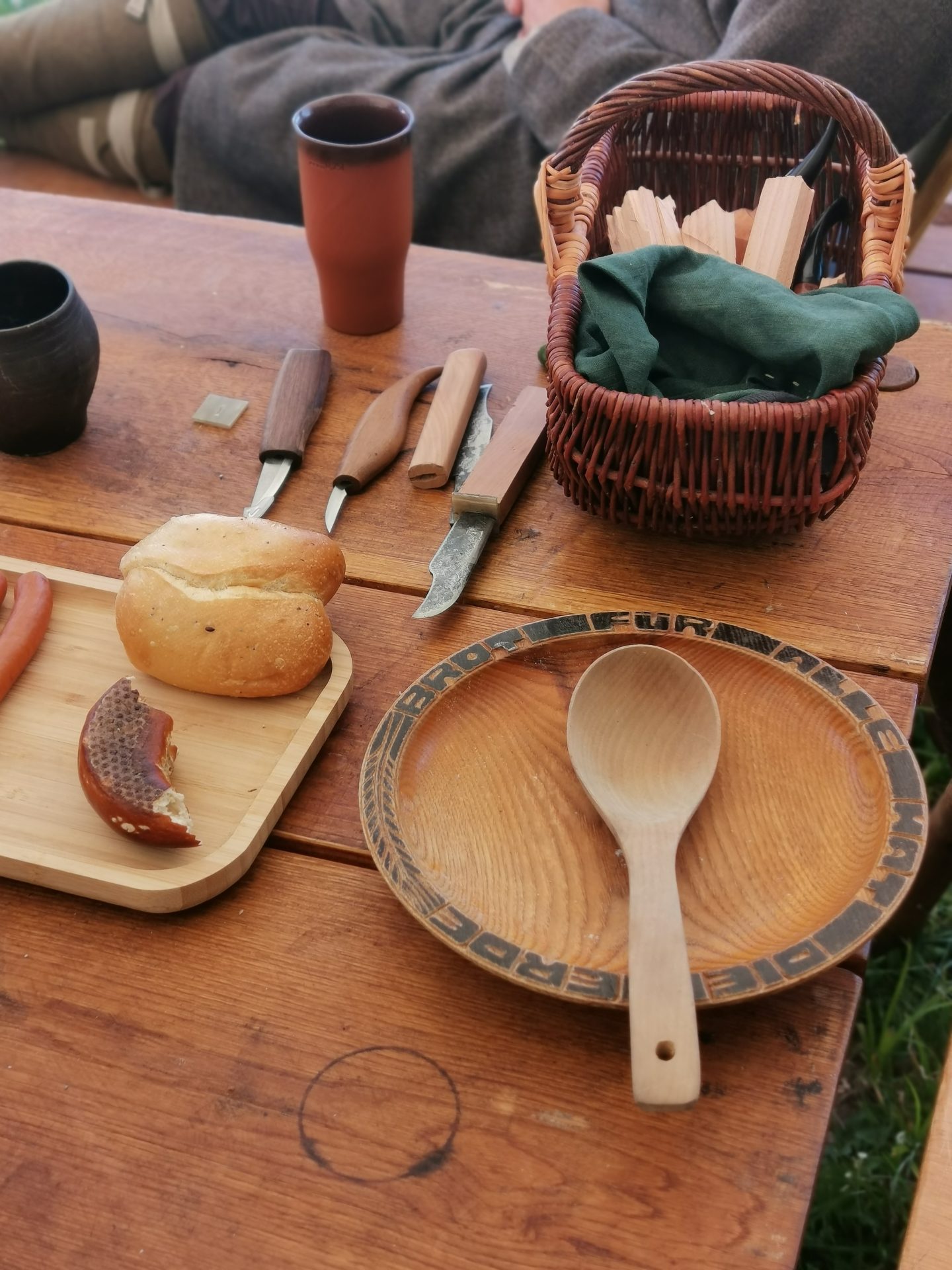 Mittelalterliches Geschirr auf einem Holztisch: Holzschale, Löffel, Messer, Brot und Tonkrug