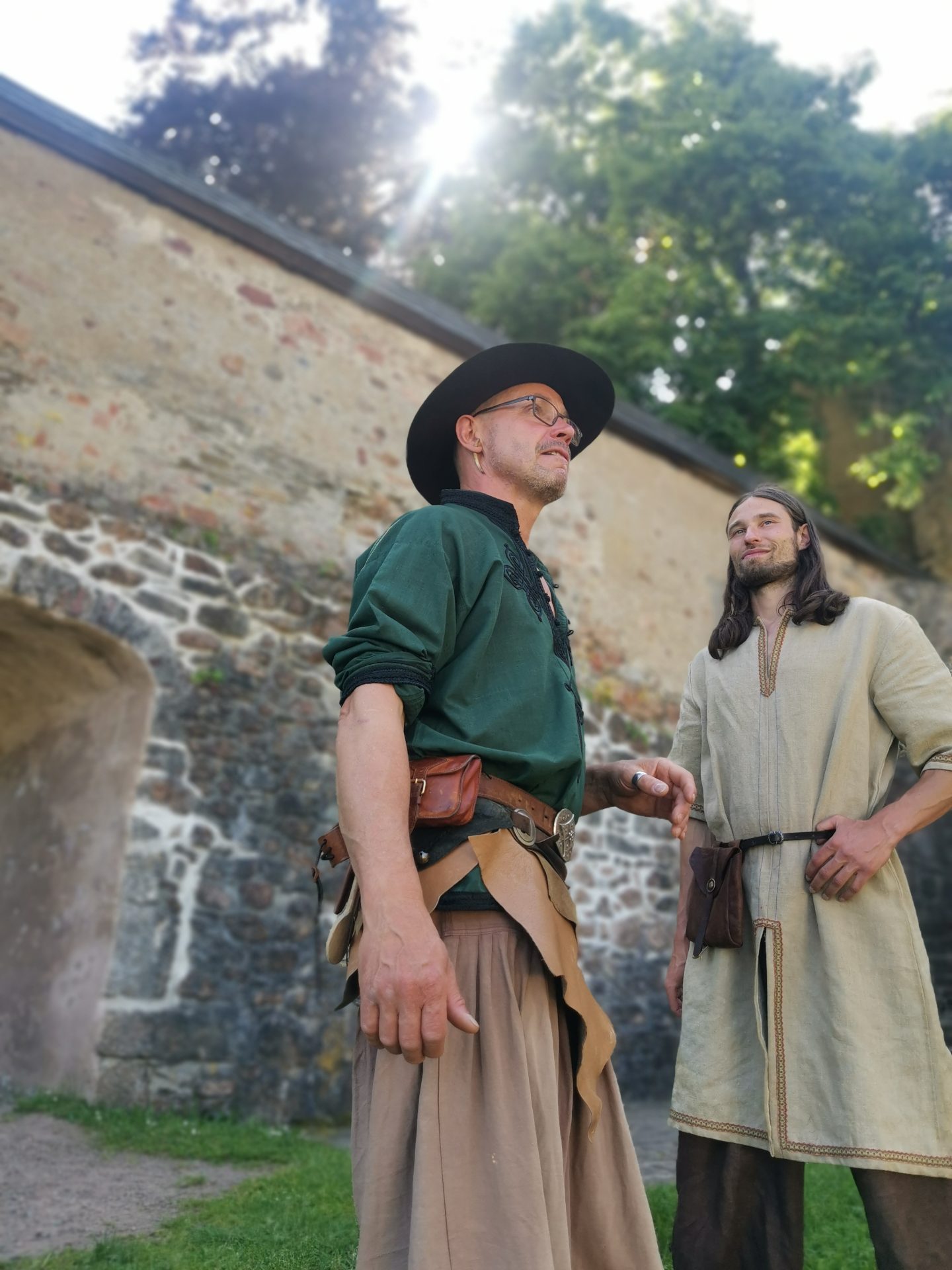 Zwei Darsteller in mittelalterlichen Gewändern im Gespräch vor historischer Burgmauer
