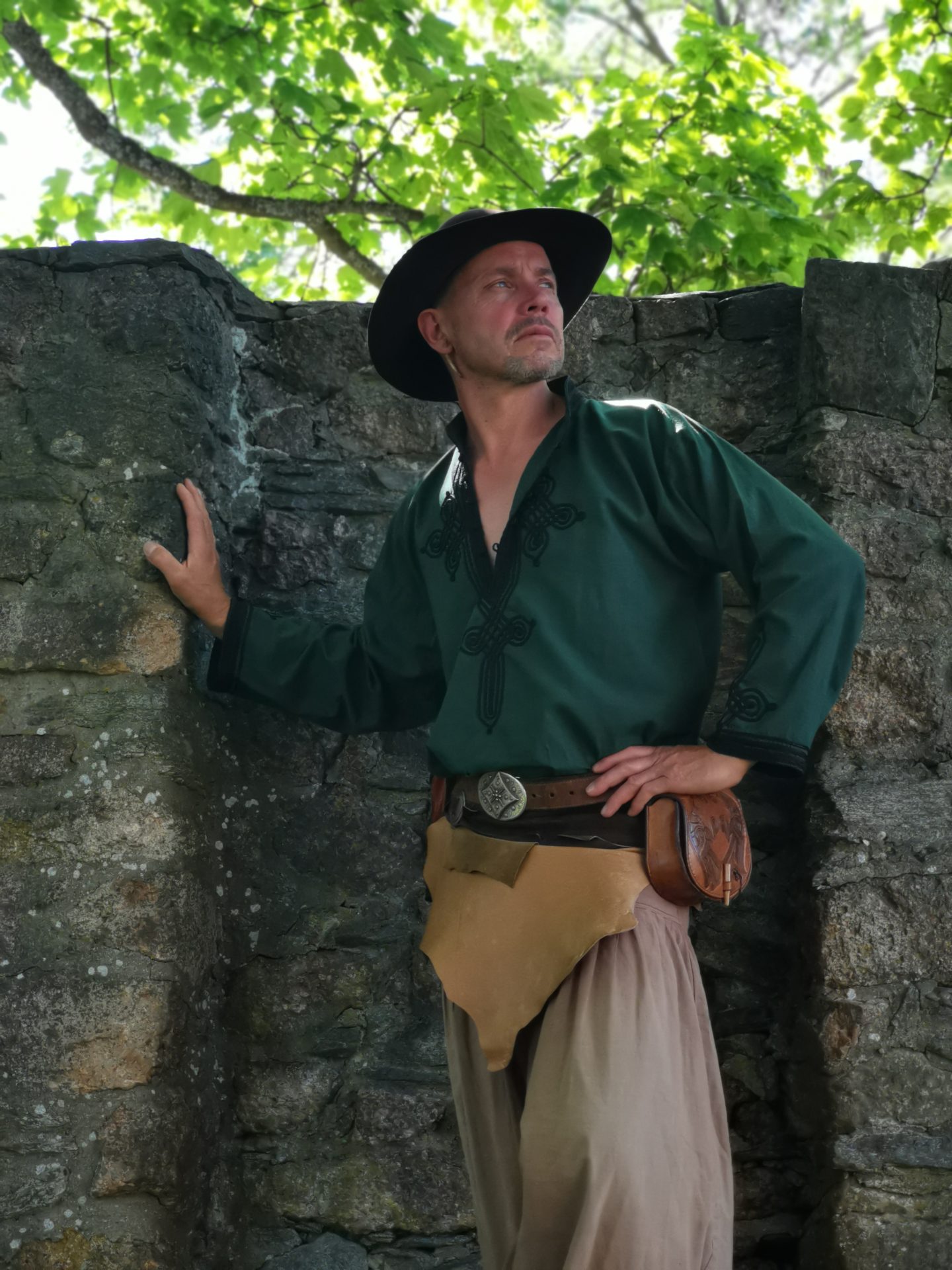 Darsteller in grünem mittelalterlichem Gewand lehnt an altem Mauerwerk und blickt nach oben